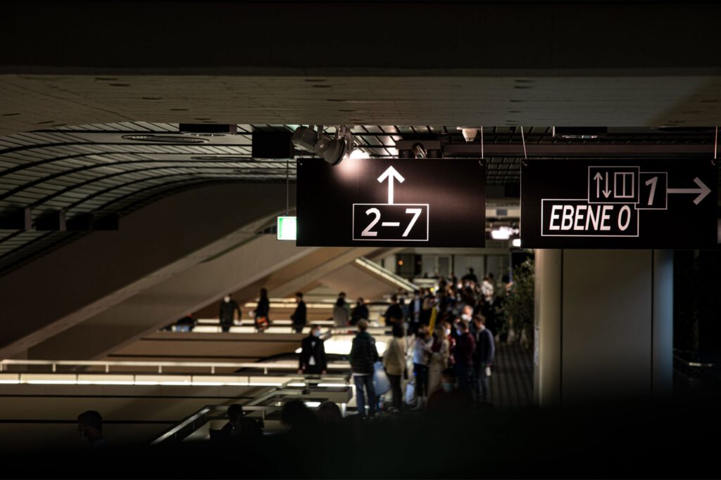 Full hall with escalators in the background. The direction sign is in focus