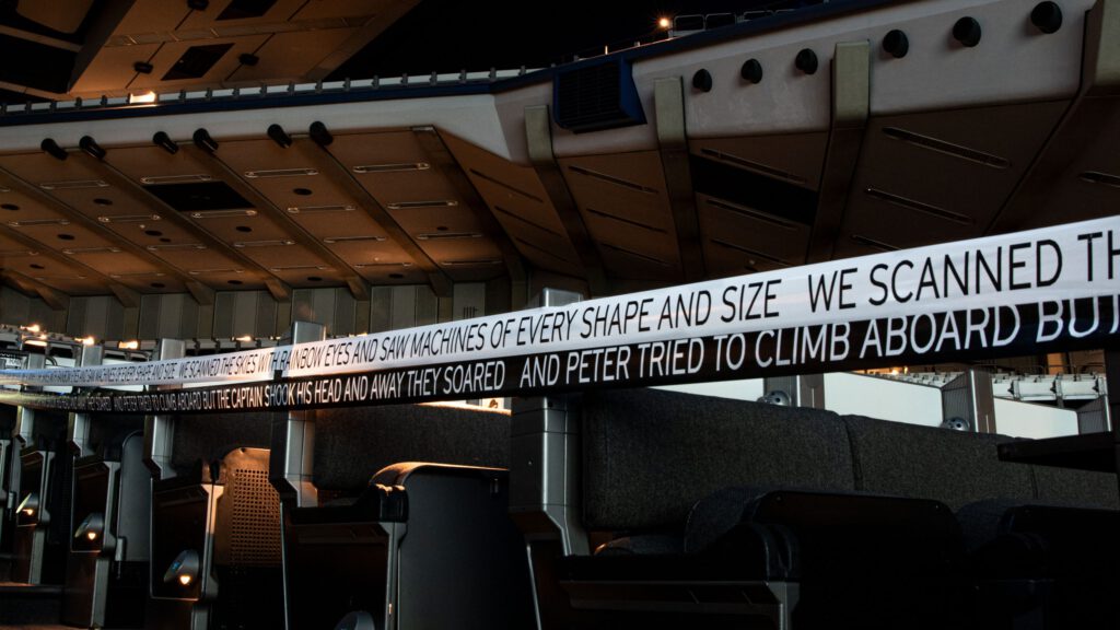 Large hall with closed-off folding seats, with an upward view. On the barrier tape is written