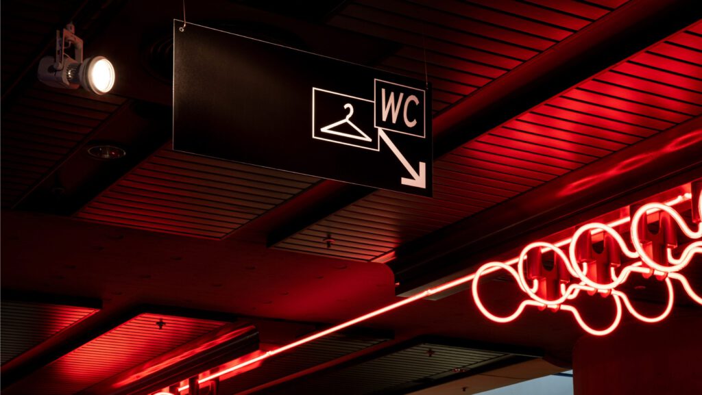 Black and white sign with checkroom and WC information. Dark room with red glow sticks