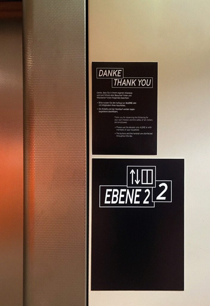 Signs next to elevator door. Acknowledgements and floor information on black and white signs.