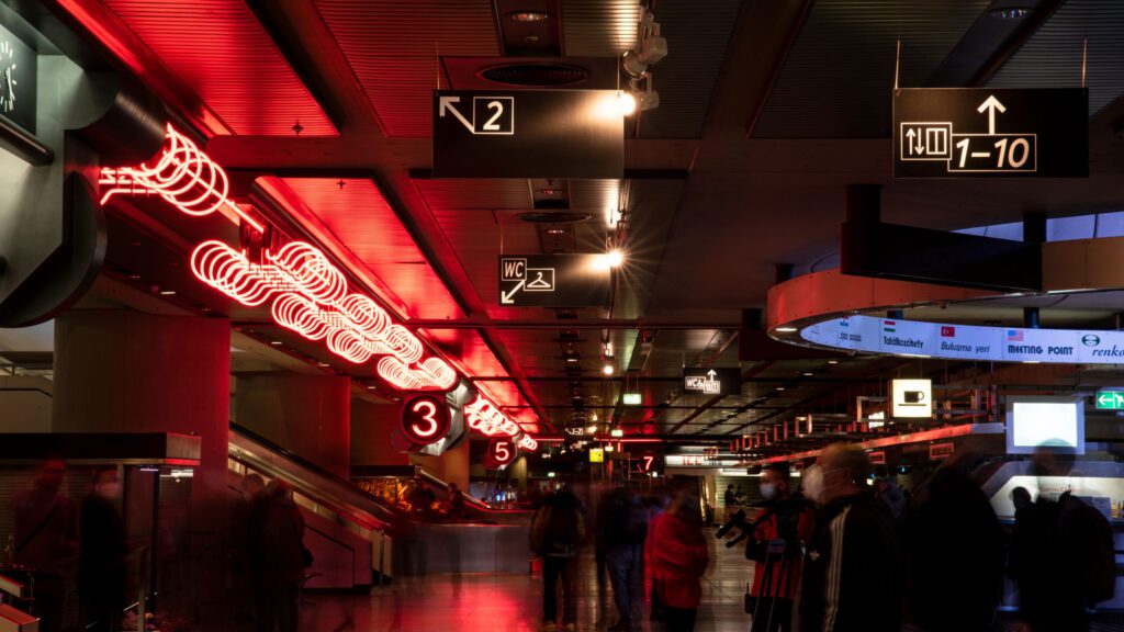 Large dark hall, passively illuminated with fluorescent tubes. Black and white signs show the way