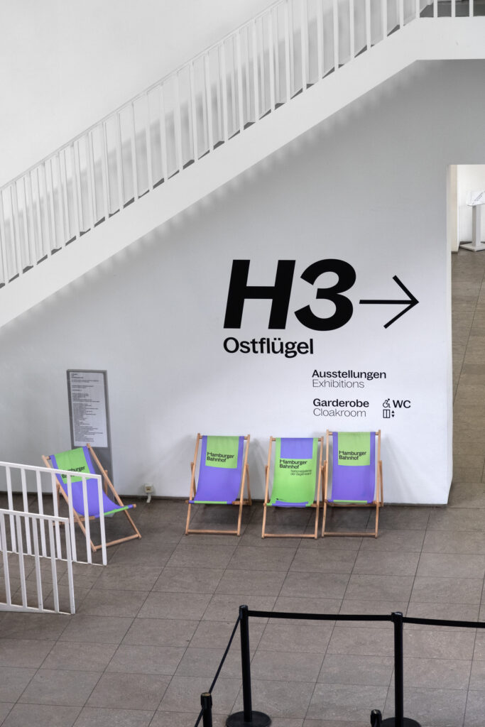 Guidance system with very large lettering and arrows. Beach chairs stand in front of it and a staircase can be seen