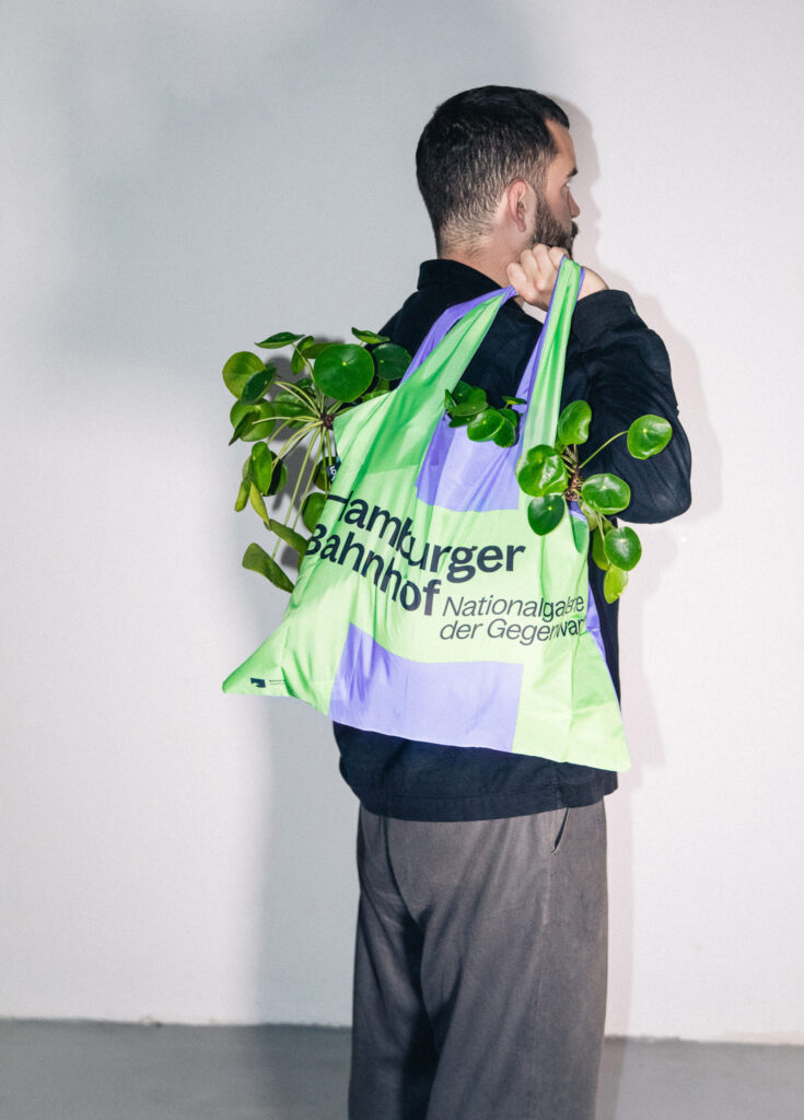 Staging of the green/purple bag with large lettering where plants are contained. Young man holds the bag in front of a white wall