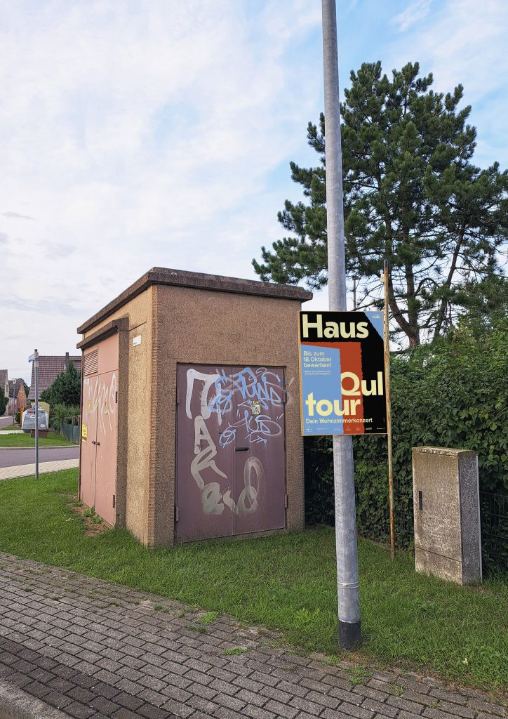 Photo of a street in the village where a colorful poster with writing hangs on a lamppost