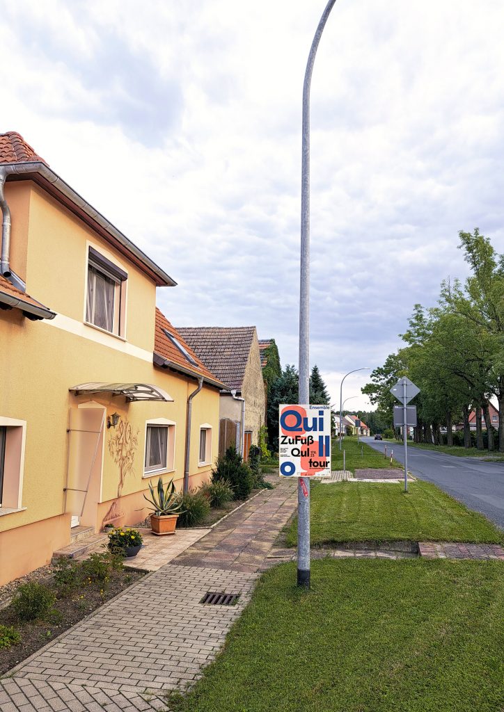 Photo of a street in the village where a colorful poster with writing hangs on a lamppost